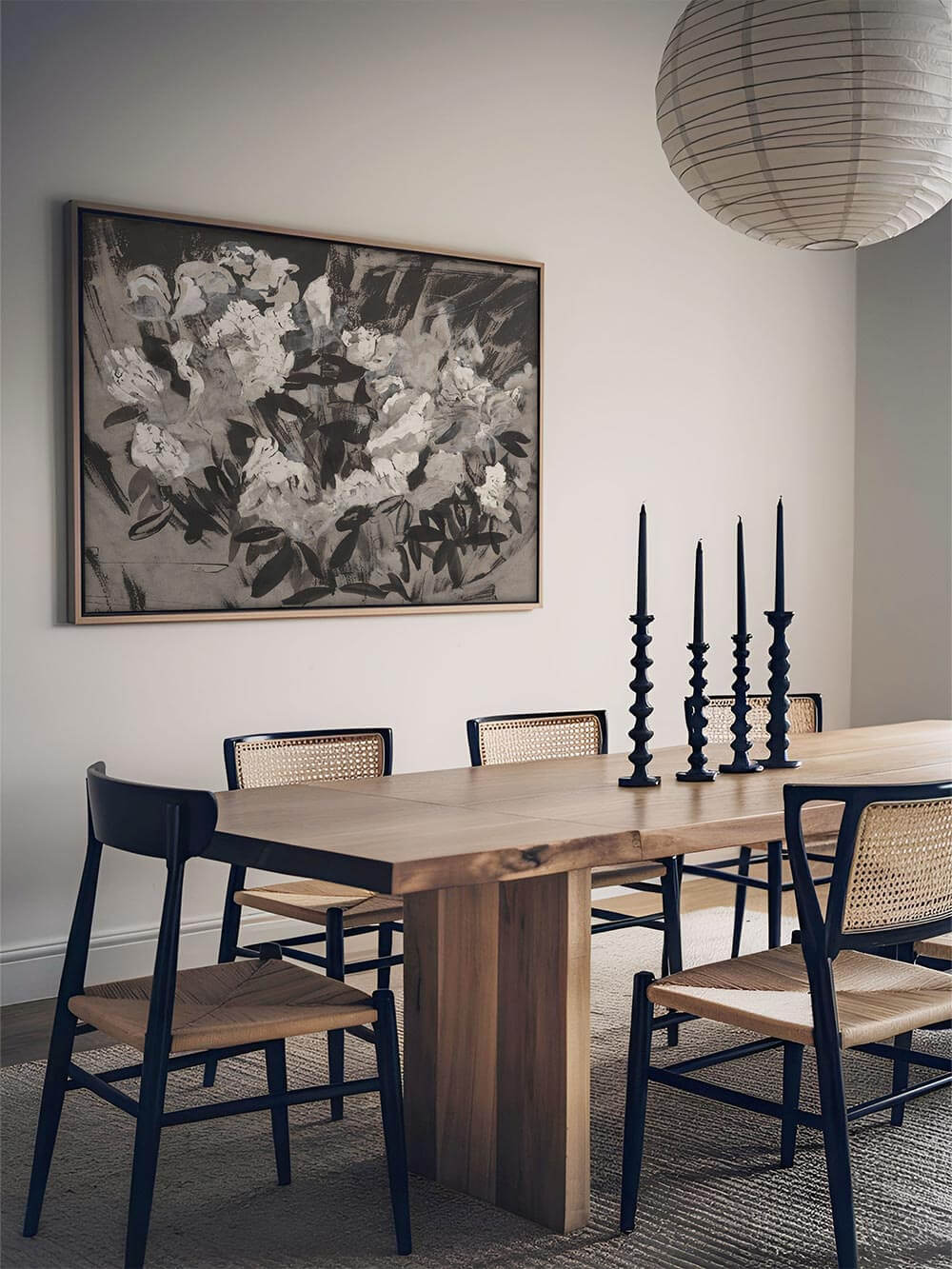 Der florale Kunstdruck hängt über einem rustikalen Esstisch mit Stühlen im Mid-Century-Stil. Die gedeckten Farben wirken harmonisch und zurückhaltend.