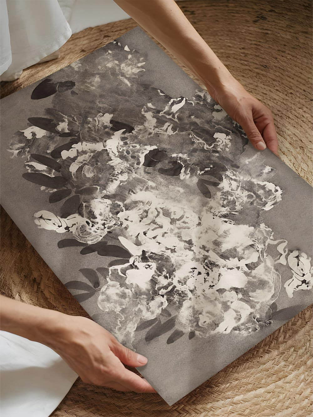 Hände, die einen schwarz-weißen floralen Tintendruck mit weichen Blütenblattstrukturen und abstrakten Pinselstrichen halten. Die Graustufenpalette und der ausdrucksstarke botanische Stil erinnern an das japanische Sumi-e und sind ideal für minimalistische oder Wabi-Sabi inspirierte Wohndekorationen.