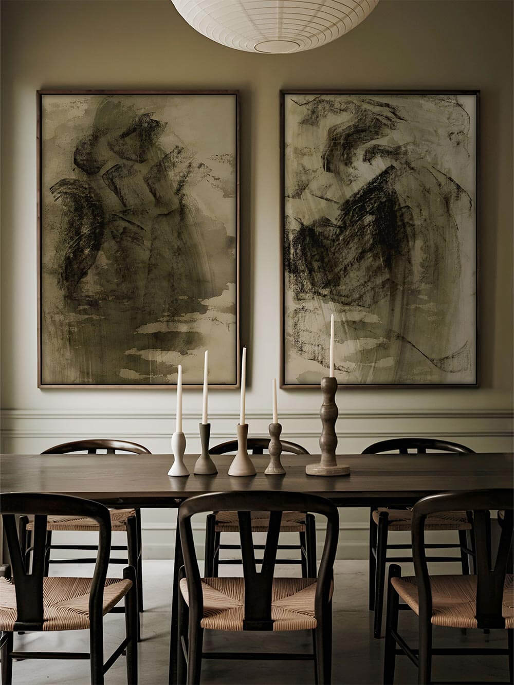 Zwei abstrakte Kunstdrucke mit dunkler Wabi-Sabi-Struktur hängen nebeneinander über einem gedeckten Esstisch. Das Wandbild-Set unterstreicht die wohnlich-edle Atmosphäre.