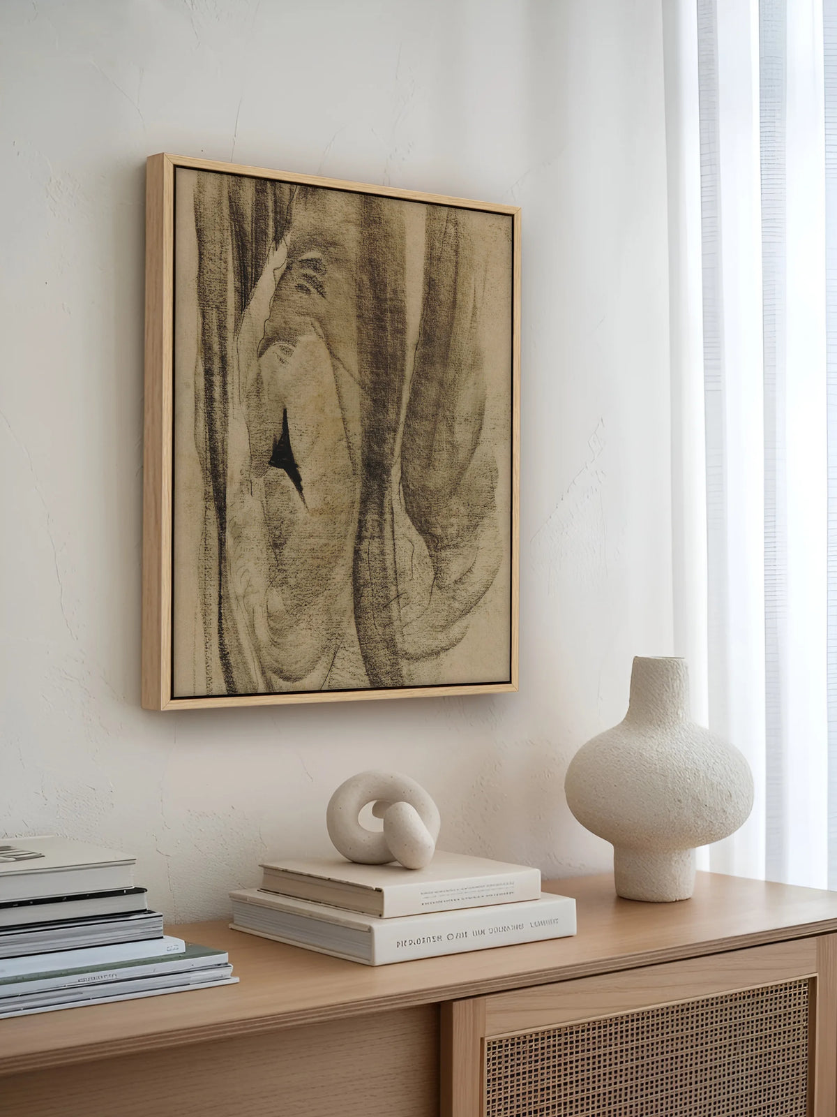 Abstraktes Leinwandbild im Naturholzrahmen über einem Sideboard mit Rattanfront, Büchern und Keramikvase. Das Wabi Sabi Wandbild fügt sich in die helle Japandi Einrichtung ein.