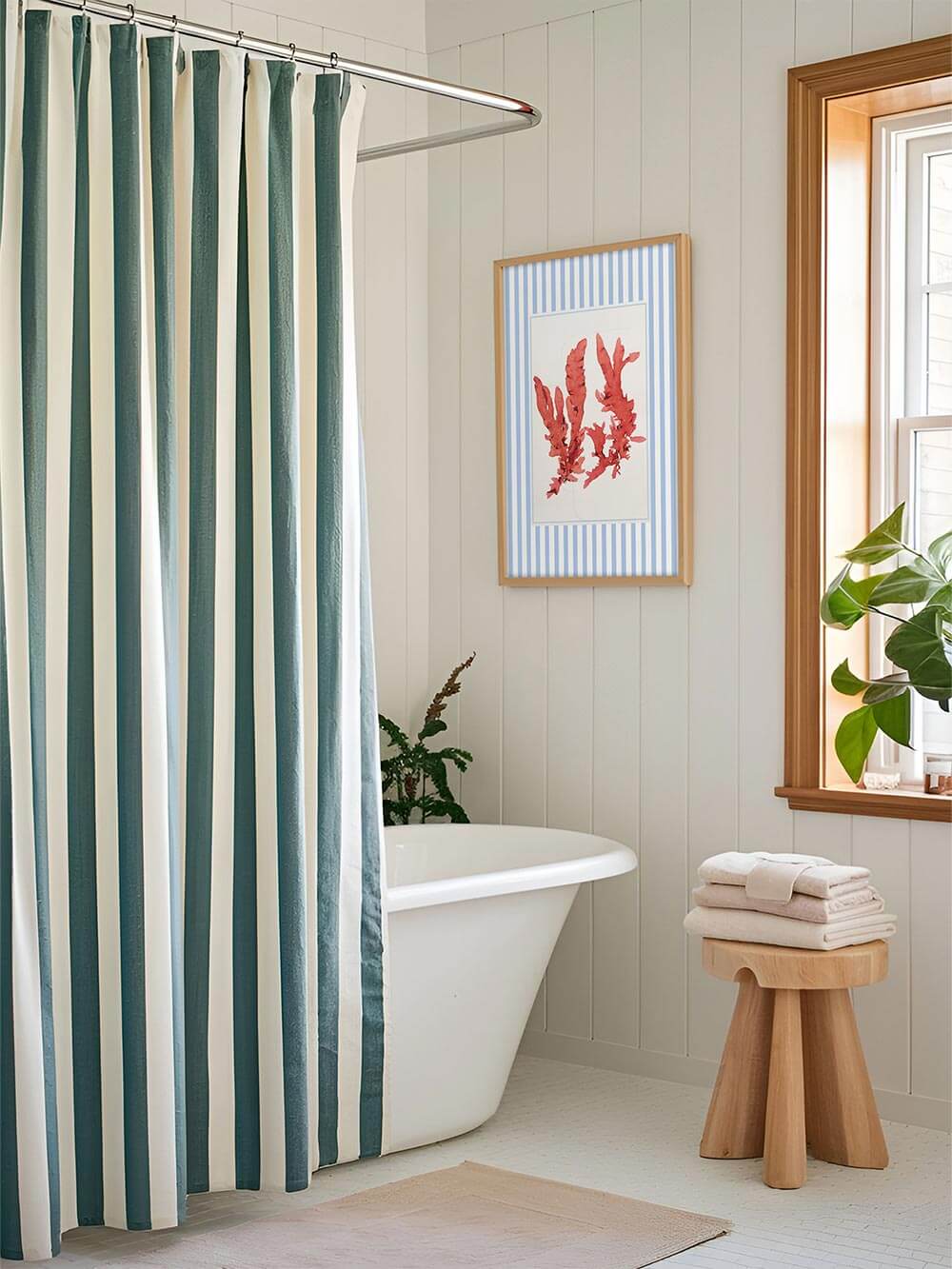 Der Algen-Kunstdruck mit Streifenrahmen hängt neben einer freistehenden Badewanne, die von einem Vorhang in Blau und Weiß ergänzt wird. Das Wandbild fügt sich stimmig in das maritime Badezimmer ein.