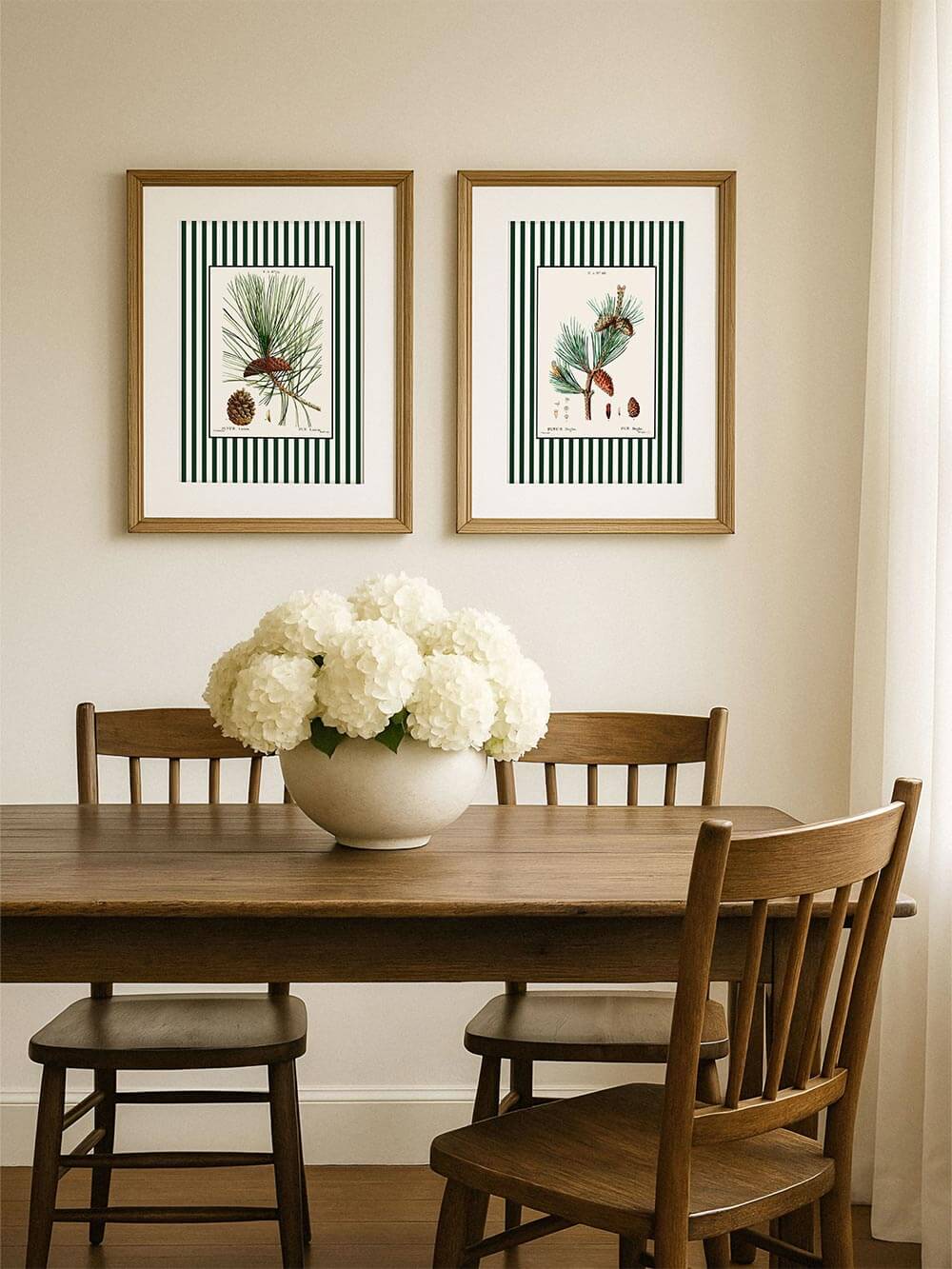 Zwei botanische Kunstdrucke mit Kiefernzweigen und Zapfen in goldenen Rahmen über einem Holztisch mit weißen Hortensien, natürliche Beige-Töne, elegantes Wandbild-Set für modernes Interieur.