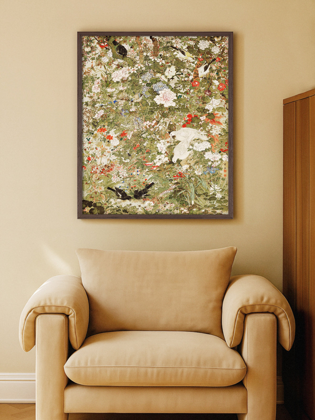 Kunstdruck nach einem japanischen Rollbild im dunklen Holzrahmen über einem beigen Sessel vor einer warmen Sandwand. Die gedämpften Grün- und Rottöne passen zu der warmen, ruhigen Einrichtung.