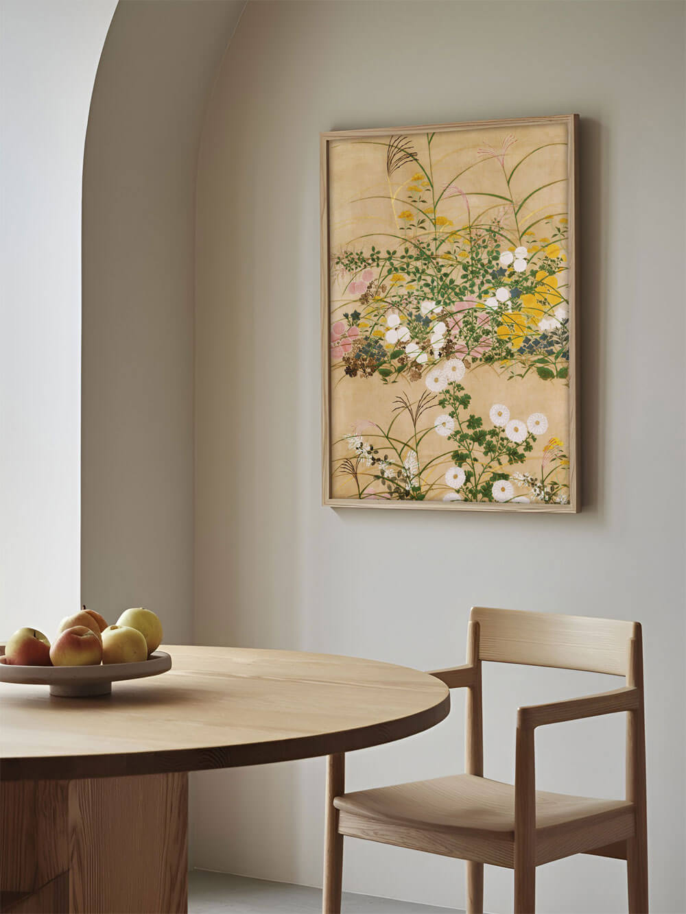 Chinoiserie-Blumendruck an einer Küchenwand über einem runden Holztisch. Das Bild zeigt eine reiche Darstellung von Blumen und Gräsern auf beigem Hintergrund, eingefasst in einen minimalistischen Holzrahmen.