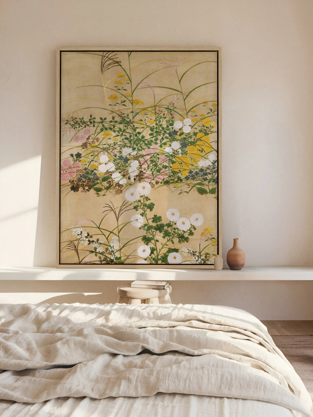 Leinwandbild mit Herbstblumen im Naturholzrahmen lehnt auf einer weißen Wandablage über einem Bett mit Leinenbettwäsche. Im Sonnenlicht wirkt das Chinoiserie Wandbild weich und hell.