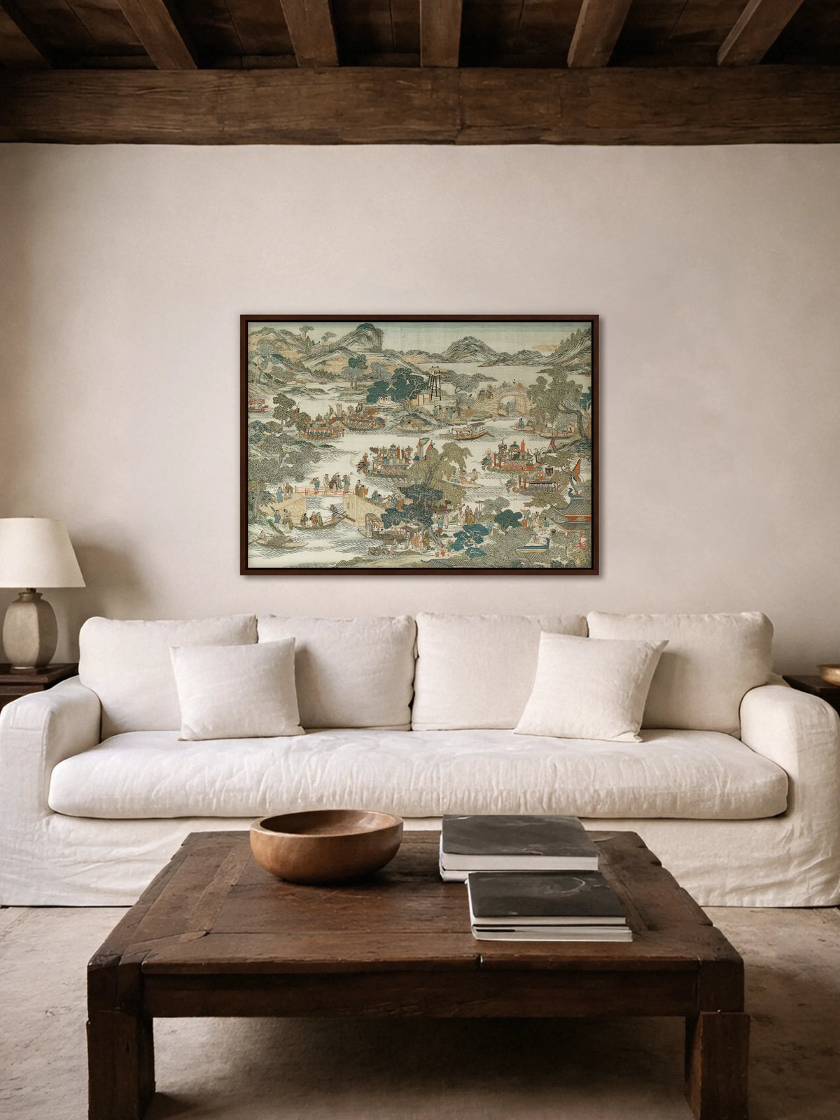 Das Chinoiserie Leinwandbild im Querformat hängt im braunen Rahmen über einem weißen Leinensofa unter dunklen Holzbalken. Davor steht ein rustikaler Couchtisch aus altem Holz mit einer Holzschale und Büchern.