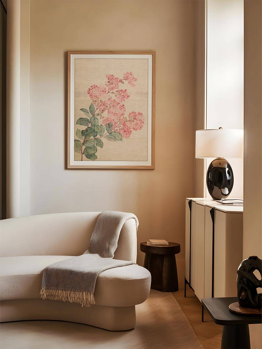 Der florale Kunstdruck mit rosa Blüten hängt in einem hellen Rahmen über einem Sofa. Warme Farben und botanische Illustration fügen sich stimmungsvoll ins Interieur ein.