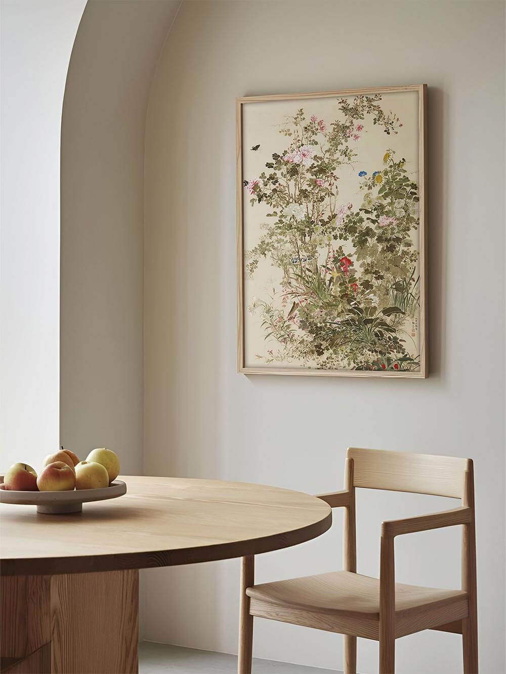 Gerahmter floraler Chinoiserie Kunstdruck hängt über einem runden Holztisch im Esszimmer. Die botanische Illustration bringt Ruhe und Eleganz in den Raum.