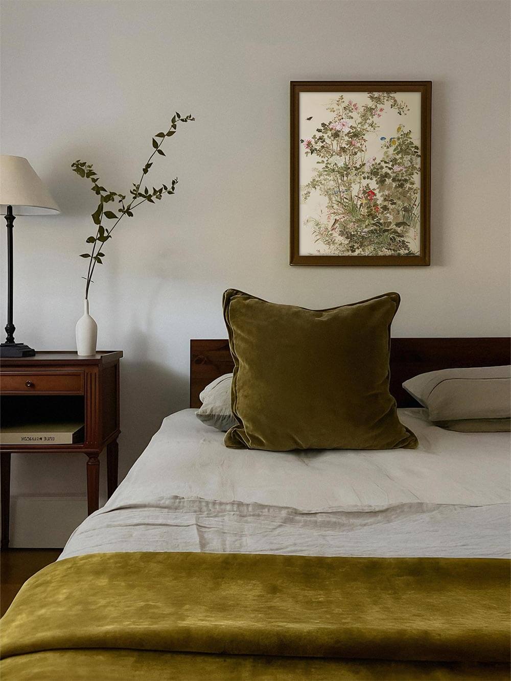 Gerahmter floraler Kunstdruck hängt über einem Bett mit grüner Tagesdecke. Die Chinoiserie Illustration ergänzt das Schlafzimmer mit einer sanften, nostalgischen Note.