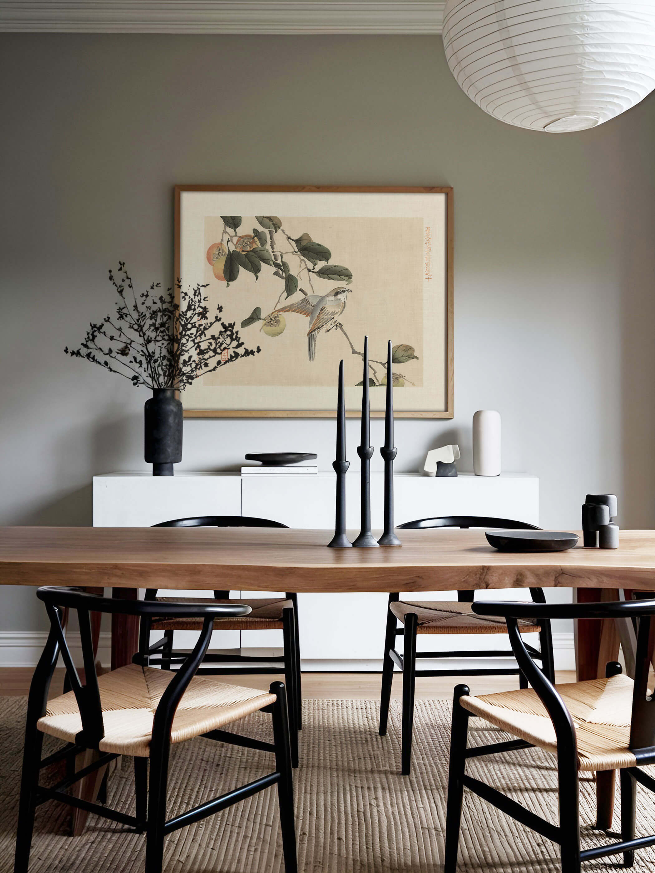 Gerahmter Chinoiserie Kunstdruck mit Vogel und Kaki-Früchten hängt über einem weißen Sideboard vor salbeigrüner Wand, umgeben von Kerzenständern und Keramik. Das warme Wandbild passt zu einem ruhigen, naturnahen Esszimmer.