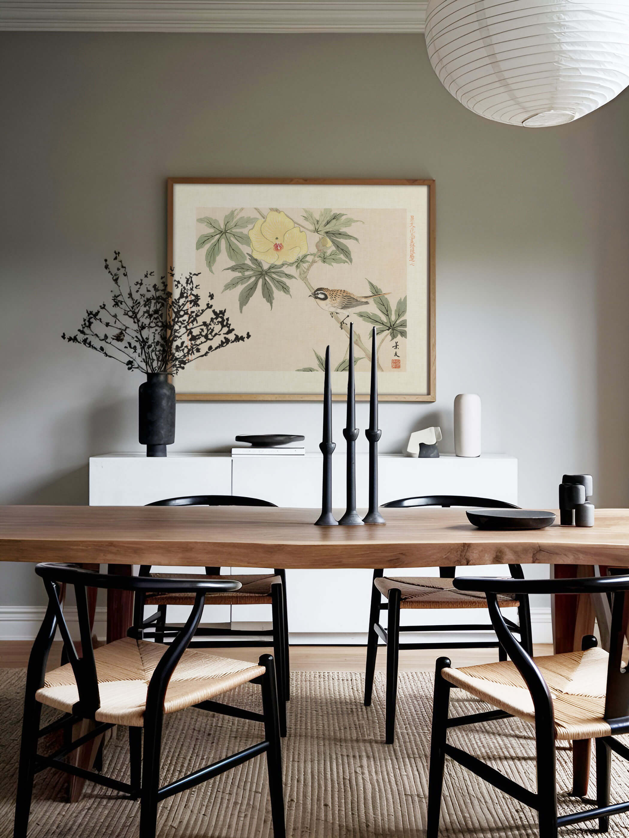Chinoiserie Kunstdruck mit Vogel und gelber Hibiskusblüte hängt über einem weißen Sideboard vor salbeigrüner Wand, umgeben von Kerzenständern und Keramik. Das sonnige Wandbild passt zu einem ruhigen, naturnahen Esszimmer.