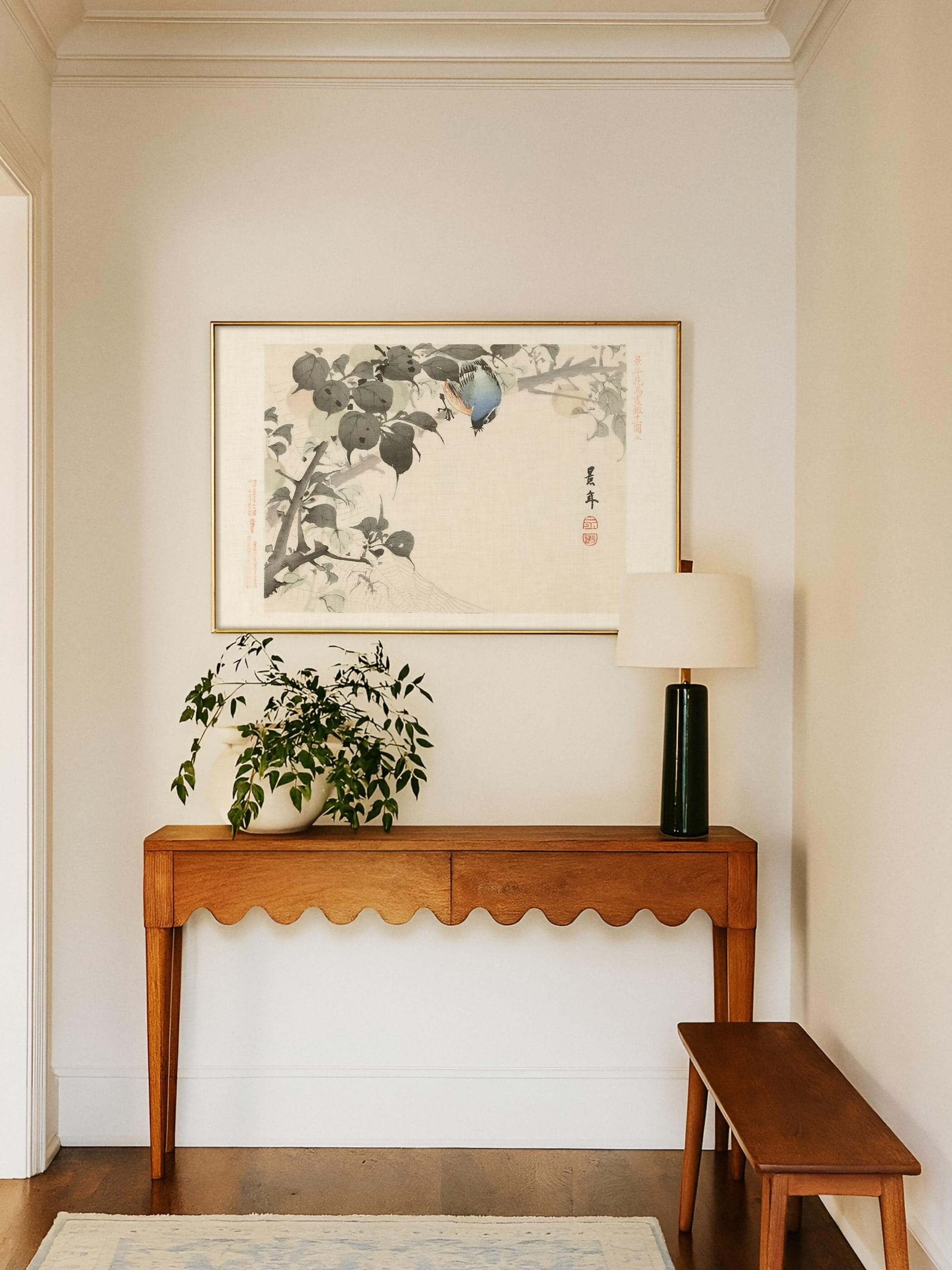 Chinoiserie Wandbild mit Vogel und Spinnennetz hängt gerahmt über einer Konsole mit Pflanze und Tischlampe im hellen Eingangsbereich. Der ruhige Kunstdruck mit farbigem Akzent verleiht dem Flur eine elegante Note.