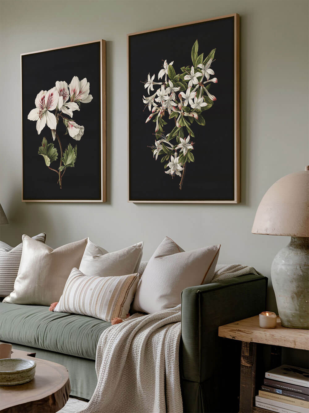 Zwei botanische Kunstdrucke hängen nebeneinander über einem olivgrünen Sofa, eingerahmt in schlichte Holzrahmen. Die weißen Blüten auf dunklem Hintergrund kontrastieren mit der sanften, beruhigenden Atmosphäre des Raums. Kissen in neutralen Farbtönen ergänzen das weiche, einladende Ambiente.
