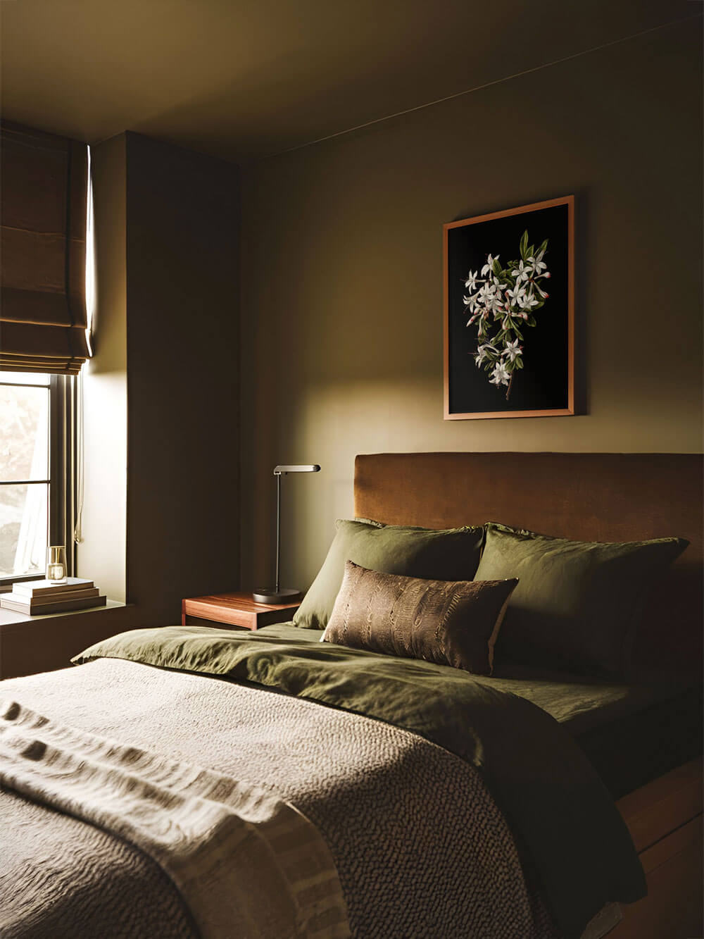 Kunstdruck mit weißen Blüten auf einem dunklen Hintergrund, aufgehängt über einem in Olivtönen gehaltenen Bett. Die Bettdecke und das Kopfteil ergänzen die beruhigende und erdige Farbpalette des Raumes, während der Kunstdruck einen eleganten Kontrast hinzufügt.