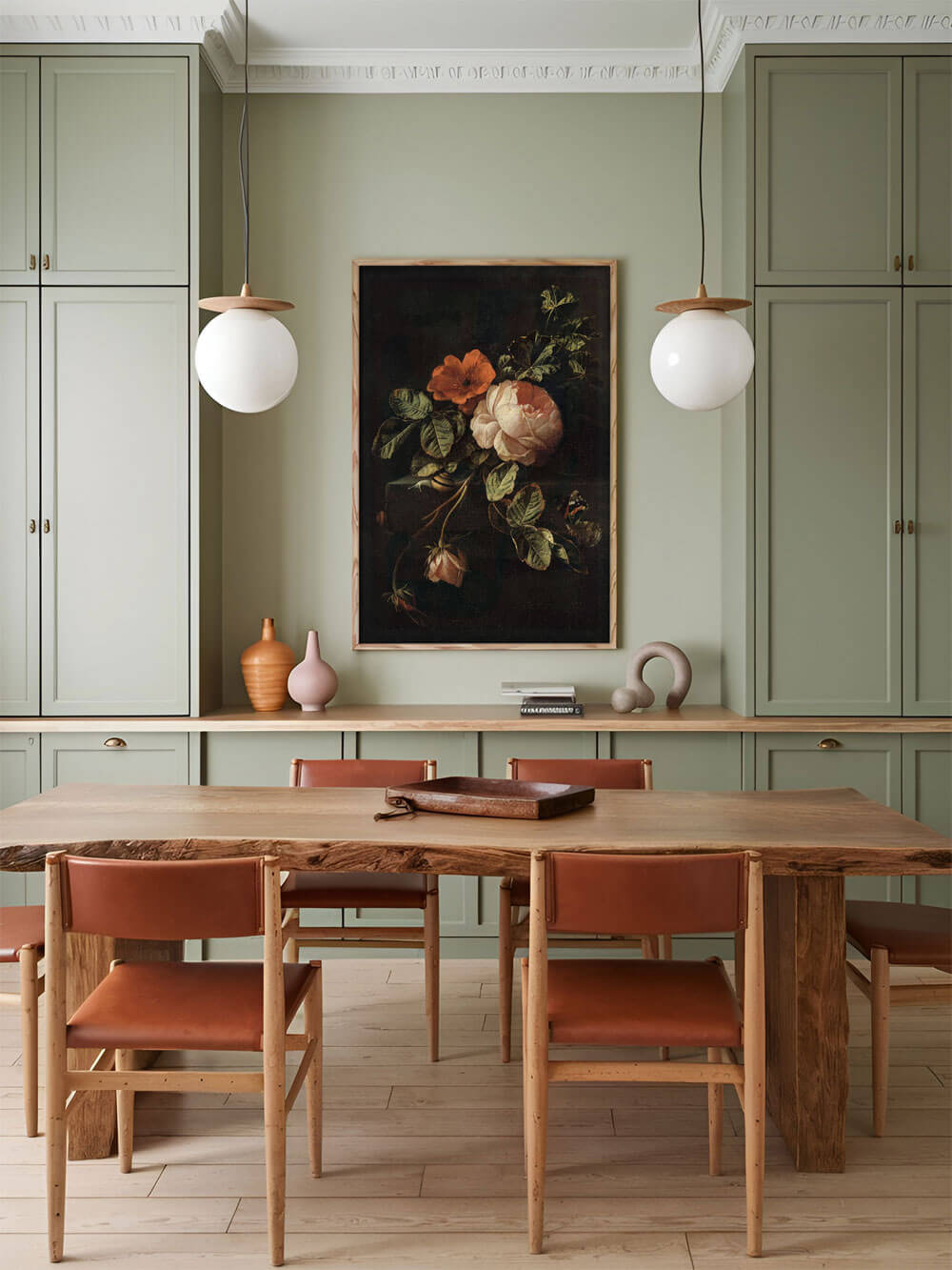 Ein dunkles, barockes Stillleben mit Rosen, das in einem gerahmten Druck an der Wand eines Esszimmers hängt. Die Szene ist in erdigen Tönen gehalten, während das dunkle Bild durch helle Holzmöbel und zarte pastellfarbene Deko-Elemente betont wird. Die Kombination aus antikem Kunststil und modernem Interior vermittelt eine harmonische Balance zwischen Tradition und Moderne.