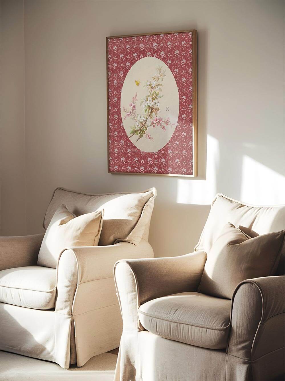 Der florale Kunstdruck mit zarten weißen und rosa Blüten hängt zwischen zwei Leinen-Sesseln im Sonnenlicht. Das Blumenmotiv hebt sich stimmungsvoll vom roten Hintergrund ab.