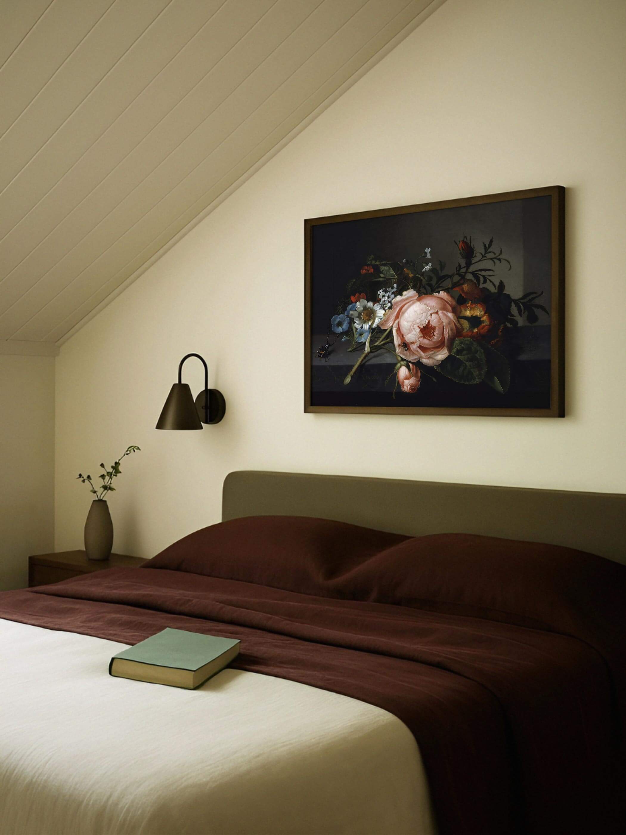 Dunkel gerahmter Kunstdruck mit Rosenzweig hängt über einem Bett mit bordeauxroter Bettwäsche unter einer schrägen Zimmerdecke. Das ruhige, dunkle Motiv fügt sich harmonisch in die warme, gedeckte Schlafzimmergestaltung ein.