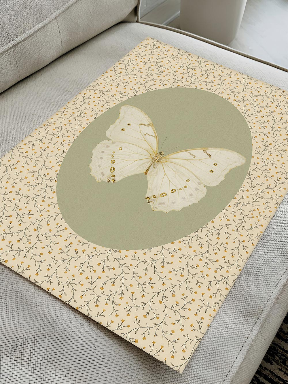 Der florale Kunstdruck mit zartem Schmetterlingsmotiv liegt auf einem hellen Sofa, die detailreiche Papiertextur und Farbgebung sind gut erkennbar.