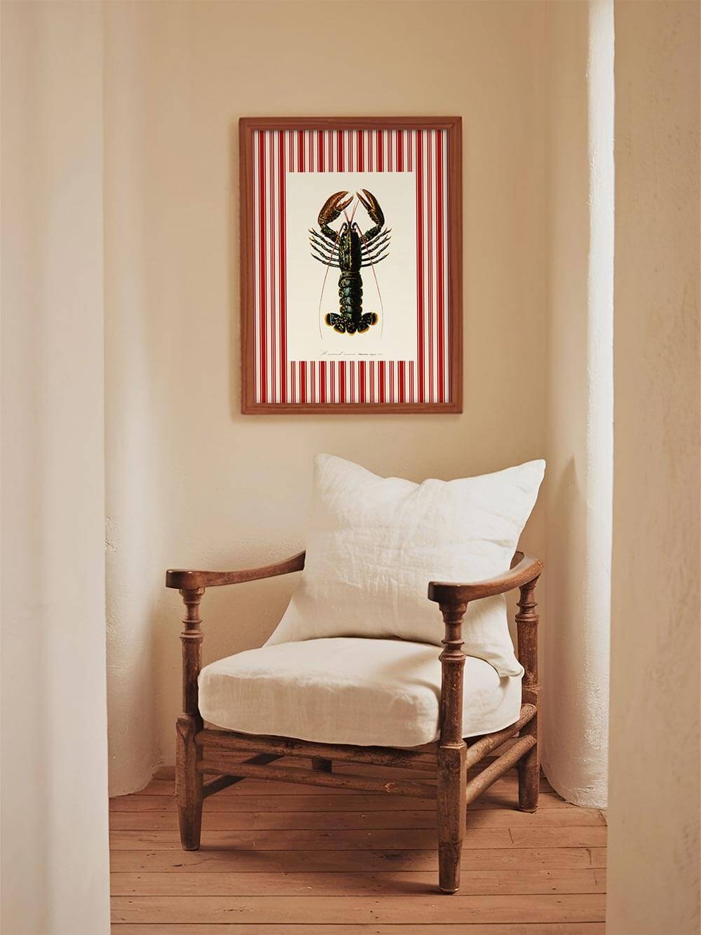 Gerahmter Kunstdruck mit Hummer-Illustration und roten Streifen hängt über einem rustikalen Lehnstuhl in einem hellen Flur mit warmem Cottage-Charme.
