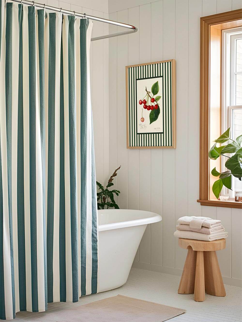 Kirsch-Kunstdruck mit grünen Streifenrahmen hängt in einem hellen Badezimmer mit freistehender Badewanne und gestreiftem Duschvorhang – ideal für botanische Badezimmerdeko.