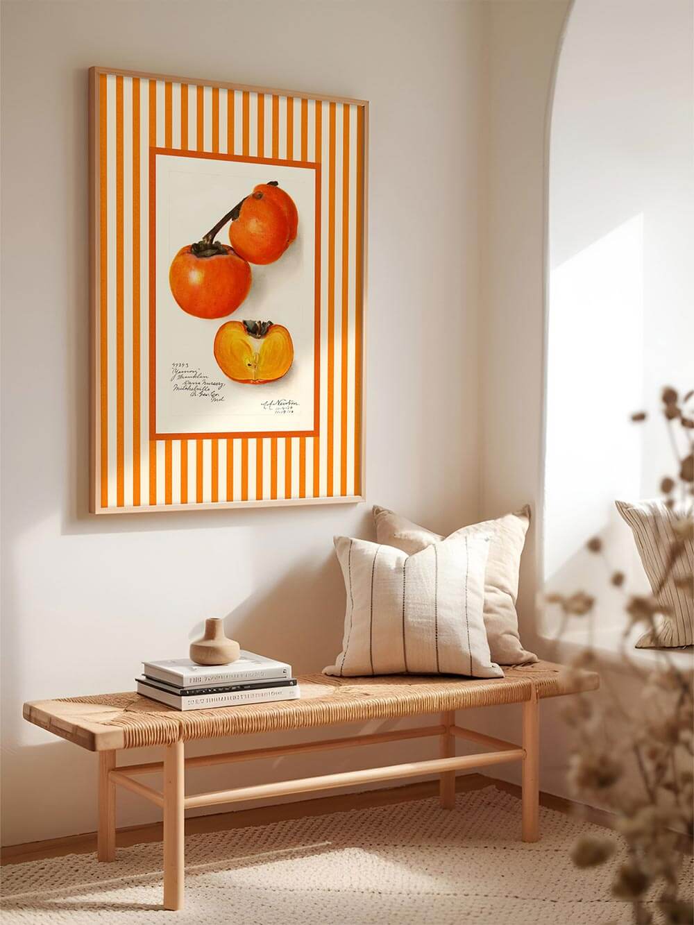 Der orange-gestreifte Kaki-Druck hängt in einem hellen Eingangsbereich über einer Holzbank mit Leinenkissen – ein stimmungsvoller Akzent für natürliche Wohnräume.