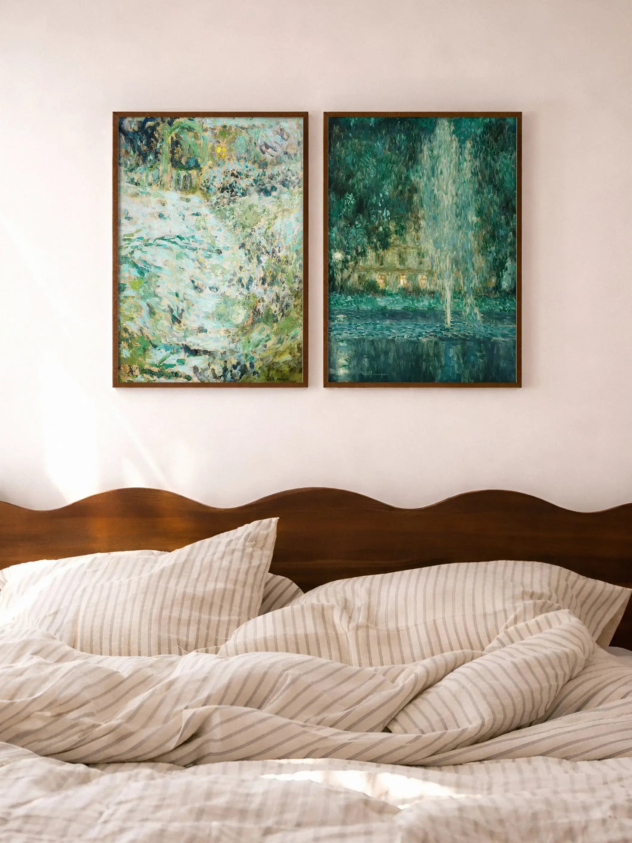 Zwei gerahmte Landschafts-Kunstdrucke in dunklem Holzrahmen hängen nebeneinander über einem Bett mit gestreifter Bettwäsche und dunklem Holz-Kopfteil. Das Bilderpaar in Grün- und Türkistönen schafft eine ruhige, naturnahe Gallery Wall im Schlafzimmer.