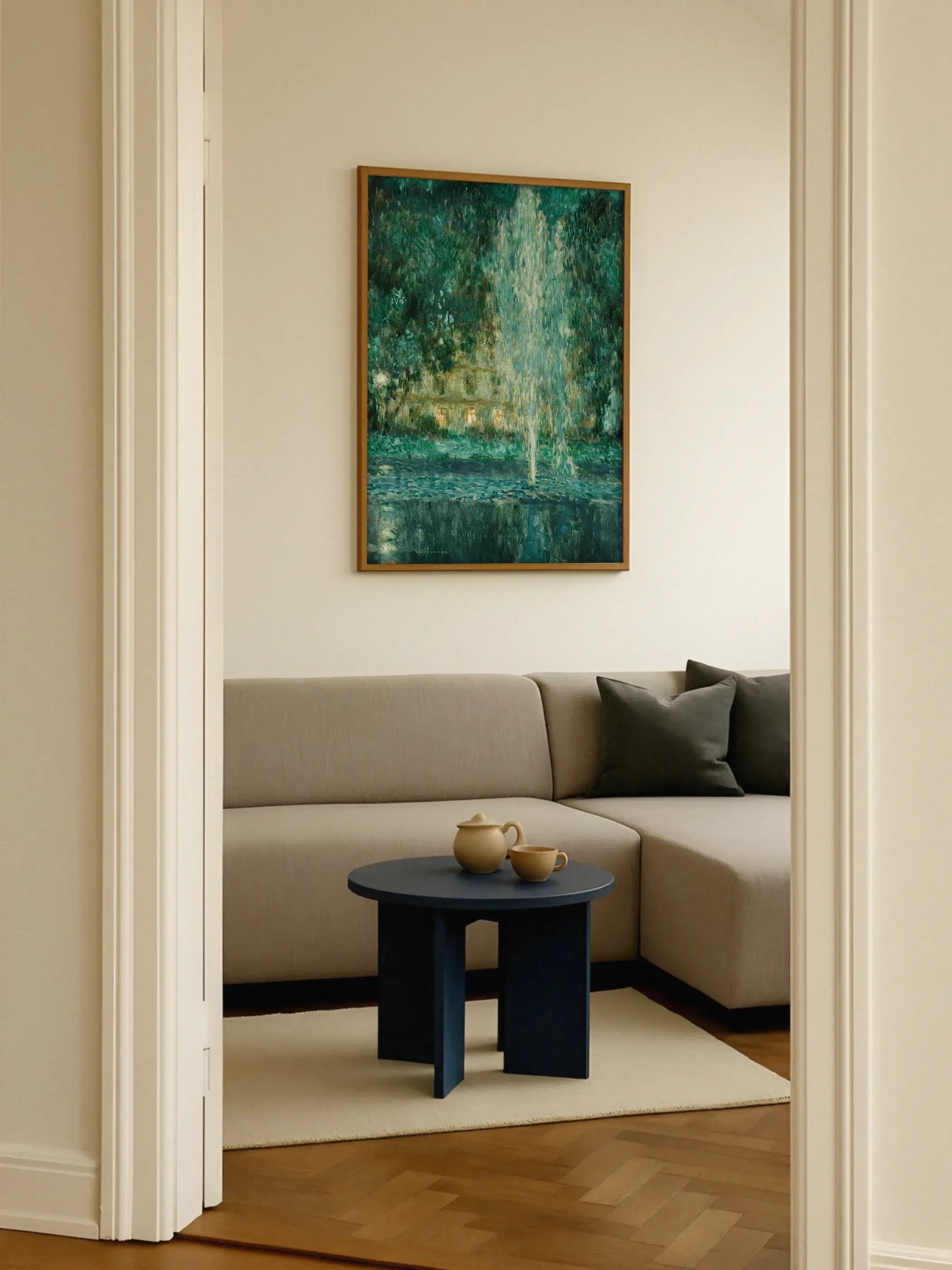 Kunstdruck mit Wasserfontäne in hellem Holzrahmen hängt an cremefarbener Wand über einem beigefarbenen Sofa mit dunklen Kissen. Das smaragdgrüne Wandbild setzt einen ruhigen Farbkontrast im modernen Wohnzimmer.