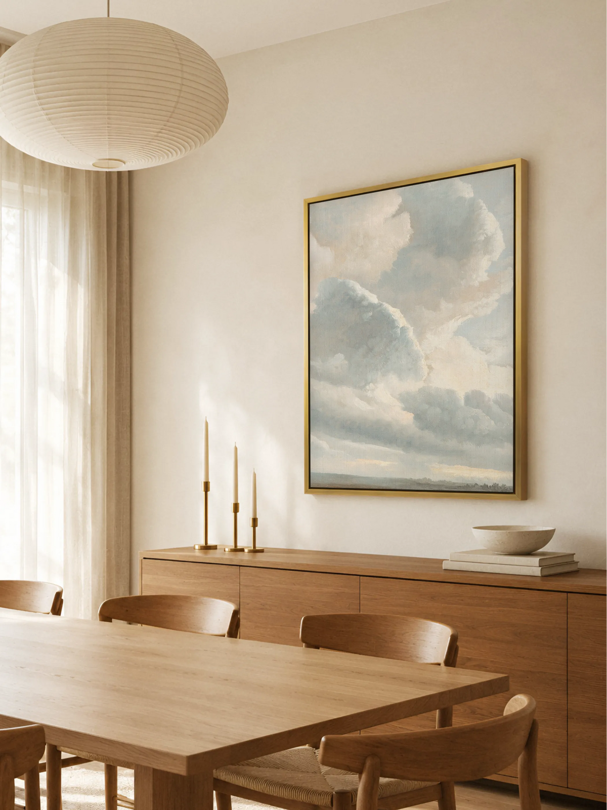 Großes Wolkenbild auf Leinwand im goldenen Rahmen über einem Sideboard aus Eichenholz im Esszimmer. Davor stehen ein Holztisch mit Stühlen und drei Messingleuchter mit Kerzen, darüber hängt eine runde Papierlampe.