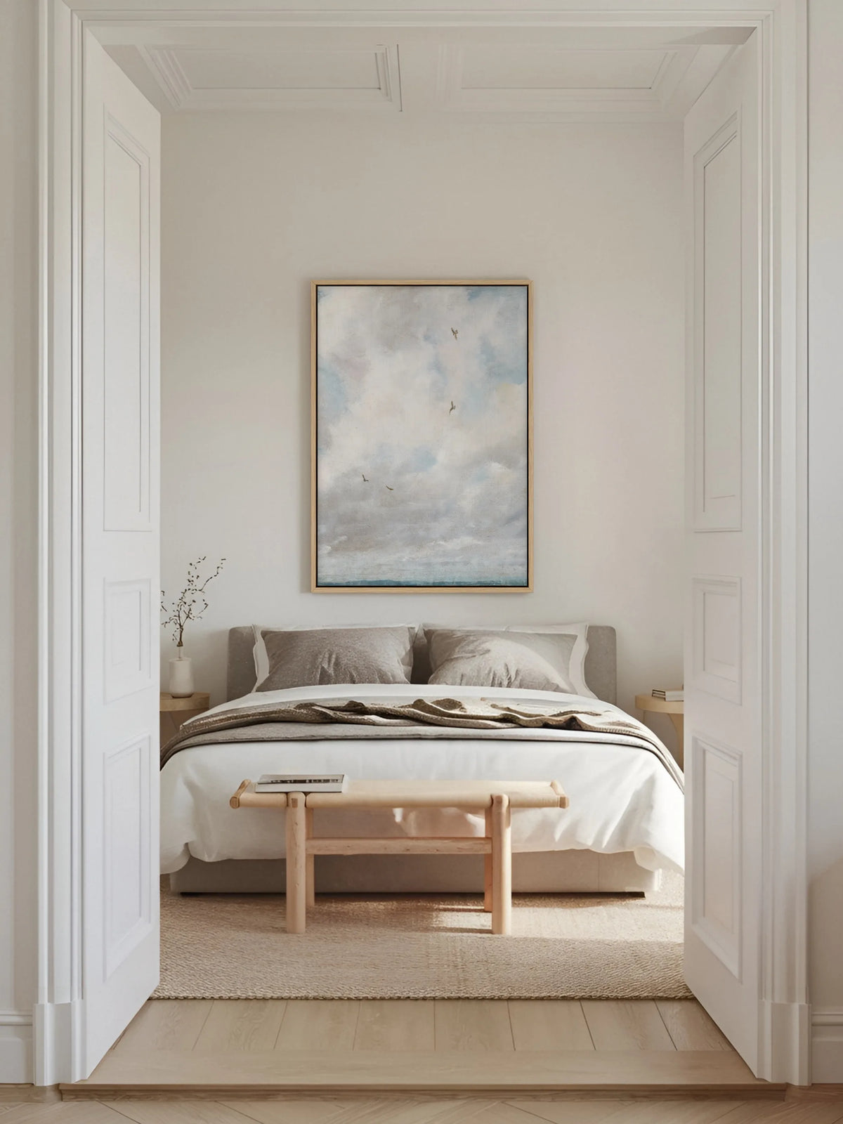 Wolken Leinwandbild im Naturholzrahmen über einem Bett mit grauer und weißer Leinenbettwäsche, gesehen durch eine weiße Flügeltür im Altbau. Vor dem Bett steht eine helle Holzbank auf einem Juteteppich.