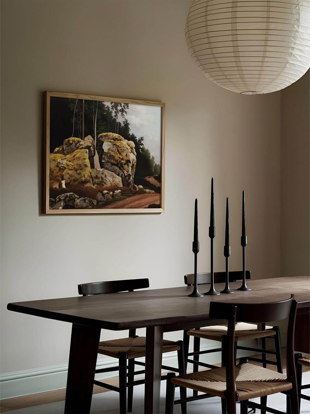 Elegantes Esszimmer mit dunklem Holztisch und skandinavischem Design, dekoriert mit einem klassischen Landschaftsgemälde. Die moosbedeckten Felsen des Kunstdrucks bringen eine natürliche, zeitlose Atmosphäre in den Raum.