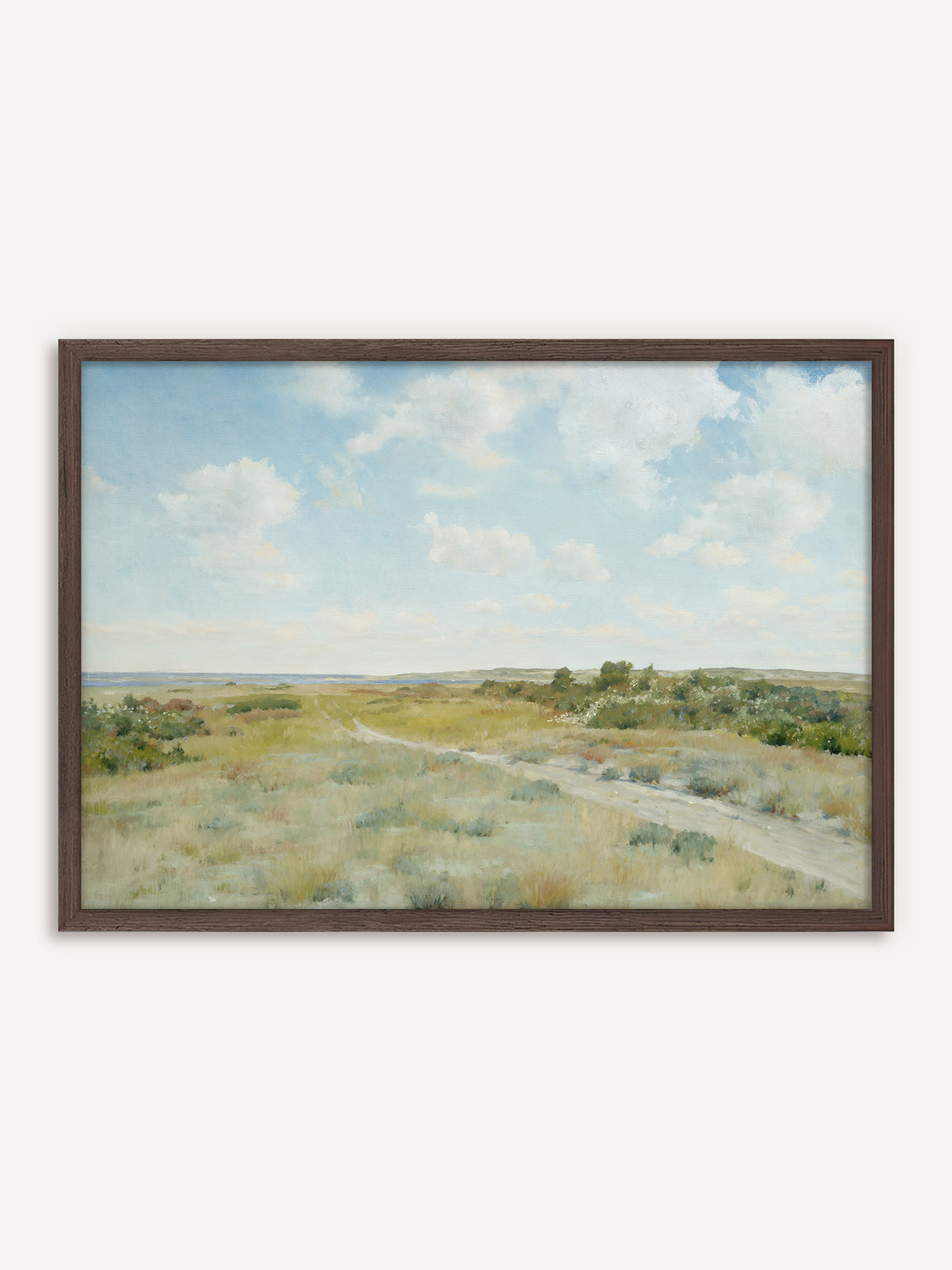 Poster, das eine Heidelandschaft mit einem sandigen Weg durch salbeigrünes Gras und blühende Büsche zeigt, am Horizont blaues Wasser unter weißen Wolken. Der Rahmen aus dunklem Holz gibt dem hellen Motiv mehr Halt und betont die rostroten Töne der Heide. #Rahmen_Dunkles Holz