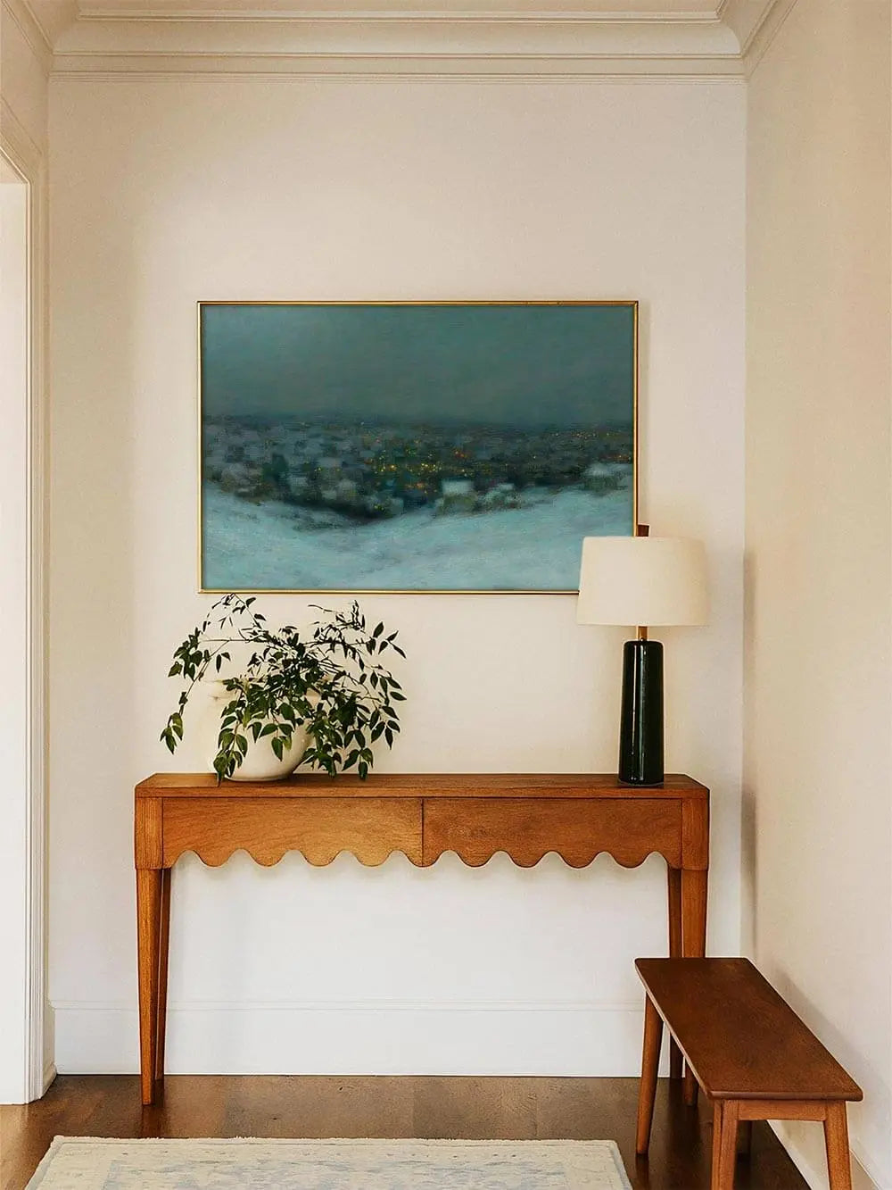 Der Vintage Kunstdruck einer winterlichen Stadtlandschaft hängt im Flur über einer schlichten Holzkonsole, seine kühlen Farbtöne wirken elegant und zeitlos.