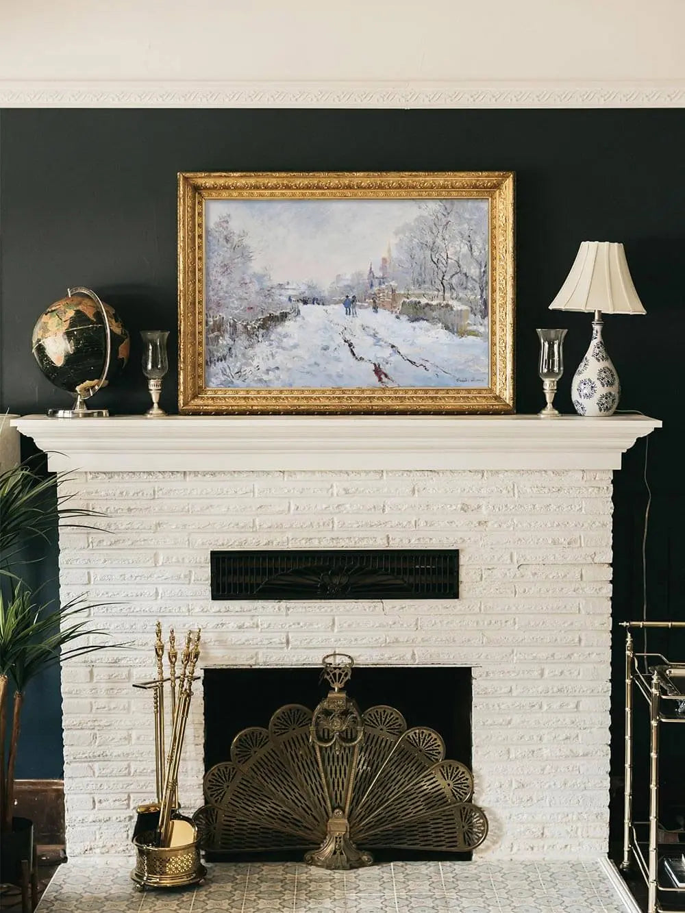 Gerahmter Winterlandschaft Kunstdruck mit verschneitem Weg und Figuren hängt über einem weißen Kamin im Wohnzimmer, die stimmungsvolle Szene betont klassische Eleganz.