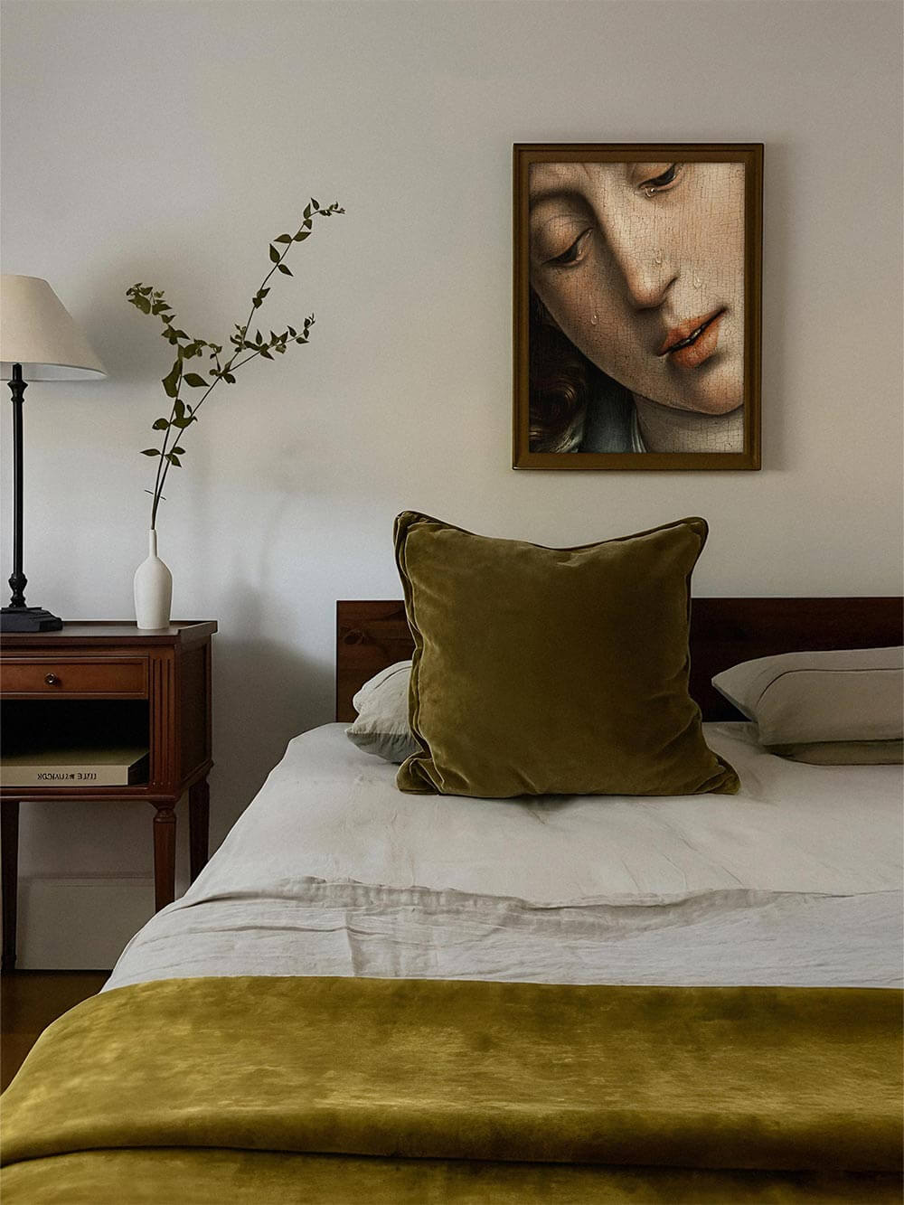 Weibliches Porträt mit Tränen im goldenen Rahmen über Bett mit olivgrüner Bettwäsche. Das Renaissance-Wandbild bringt emotionale Tiefe und zarte Eleganz in moderne Schlafzimmergestaltung.