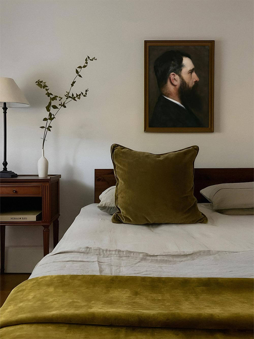 Gerahmter Kunstdruck mit Männerporträt über Bett mit goldgrünen Textilien und minimalistischer Einrichtung. Harmonische Farbstimmung – perfekt für ruhige, elegante Schlafzimmergestaltung.