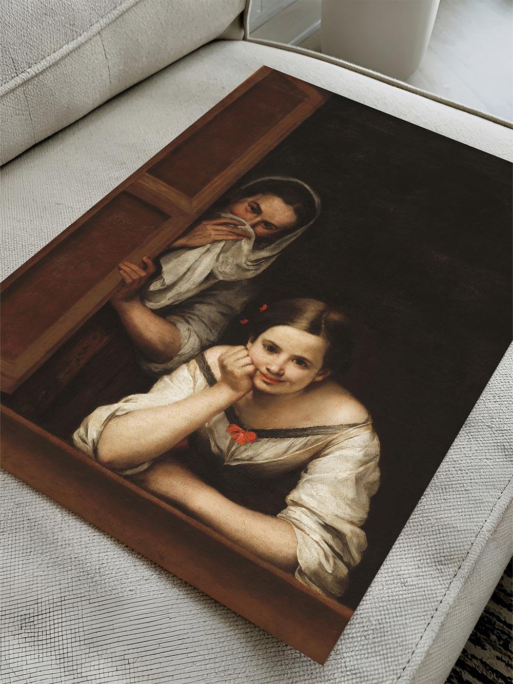 Der Vintage-Kunstdruck liegt ungerahmt auf einem hellen Sofa. Die lebendige Mimik der Figuren und die gemalte Fensterrahmung treten detailreich hervor.