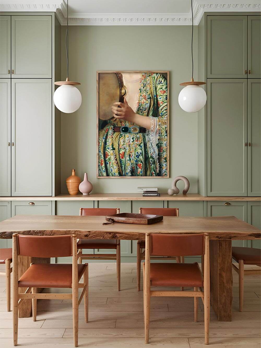 Esszimmer-Szene mit Wandkunst: Ein Kunstdruck mit einem farbenfrohen, ornamentalen Kleid und Tamburin, gerahmt an einer grünen Wand in einem stilvollen Esszimmer mit Holzmöbeln und Lederstühlen.