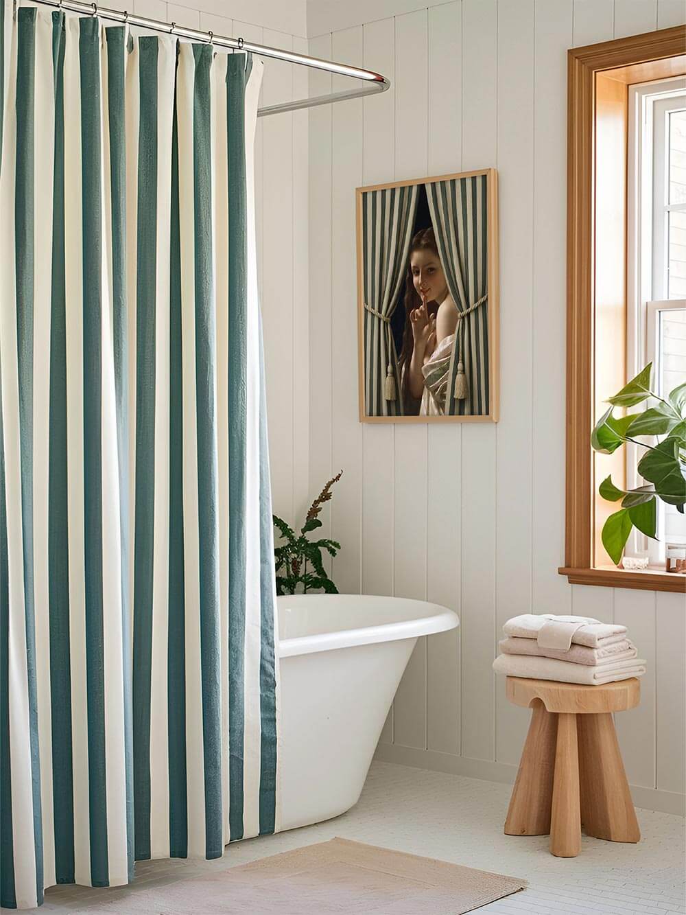 Der Vintage-Kunstdruck mit Vorhangrahmen hängt über einer freistehenden Badewanne, die gestreiften Elemente verbinden sich harmonisch mit dem Duschvorhang.