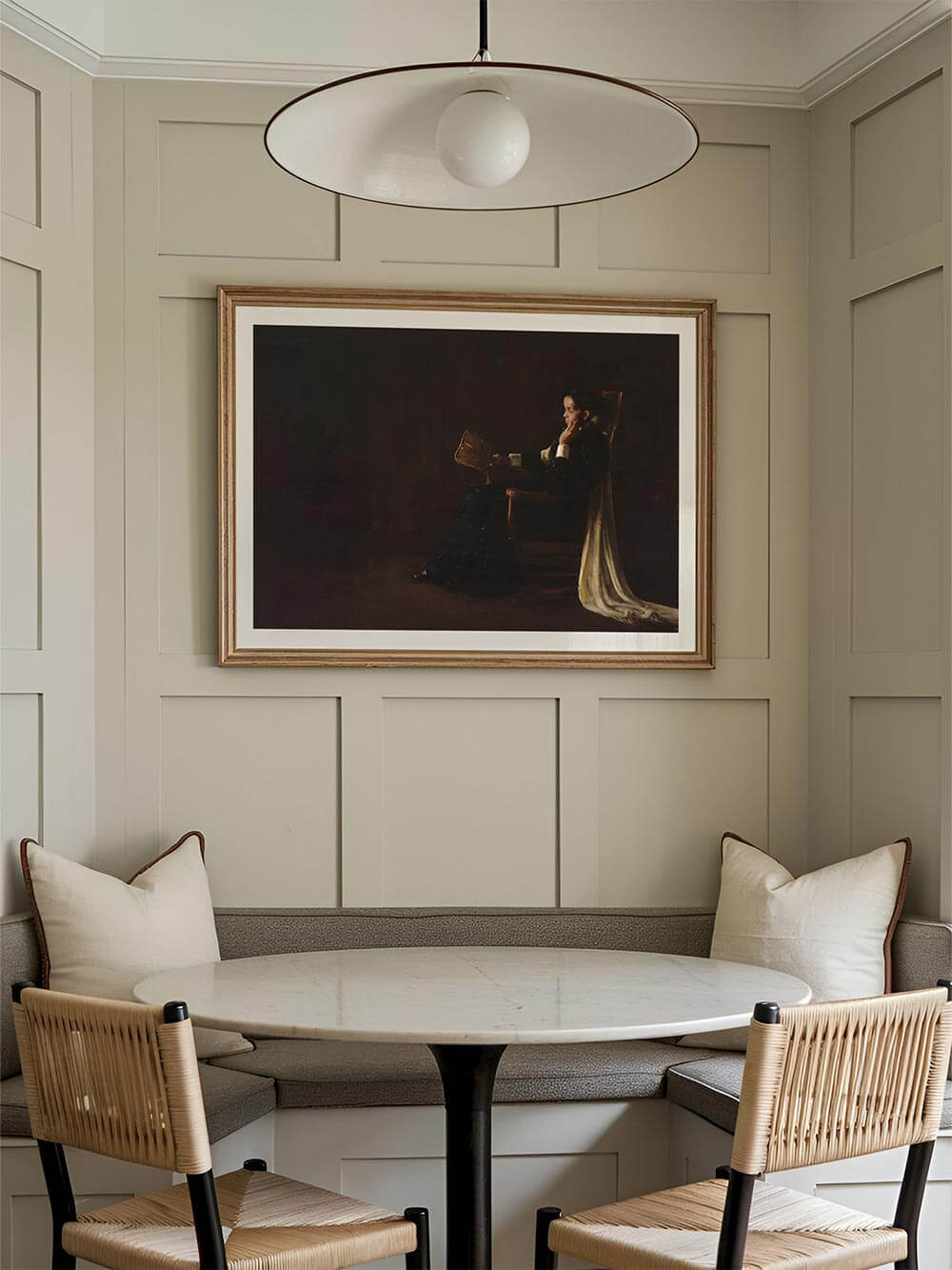 Großformatiger Kunstdruck mit dunklem, stimmungsvollem Frauenporträt hängt über einer runden Essnische mit gepolsterter Bank und Holzstühlen. Die gedeckten Farben und das gedämpfte Licht schaffen eine ruhige, elegante Atmosphäre für Esszimmer oder Küche.