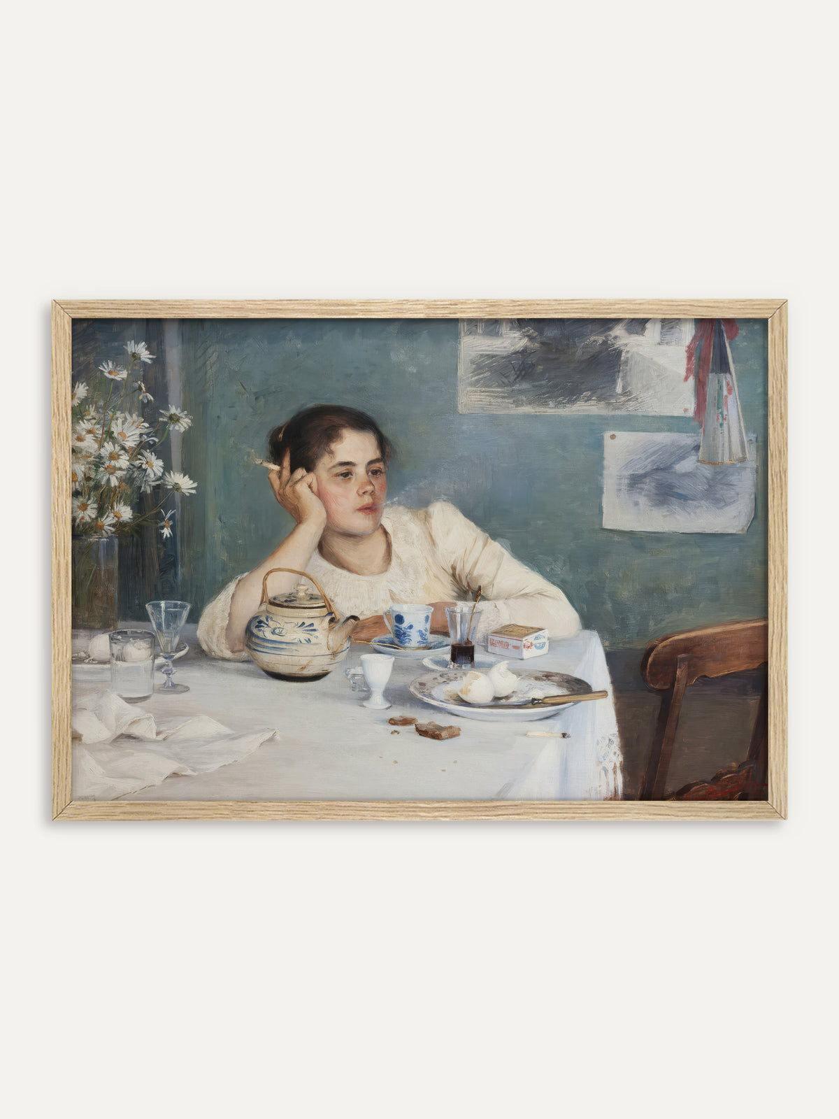 Kunstdruck, der eine junge Frau in weißer Bluse zeigt, die nach dem Frühstück mit einer Zigarette den Kopf in die Hand stützt, vor ihr ein Tisch mit blau-weißer Teekanne, Eierschalen und einem Strauß Margeriten vor blaugrüner Wand. Im Rahmen aus hellem Holz wirkt die Szene frisch wie ein Sommermorgen. #Rahmen_Helles Holz
