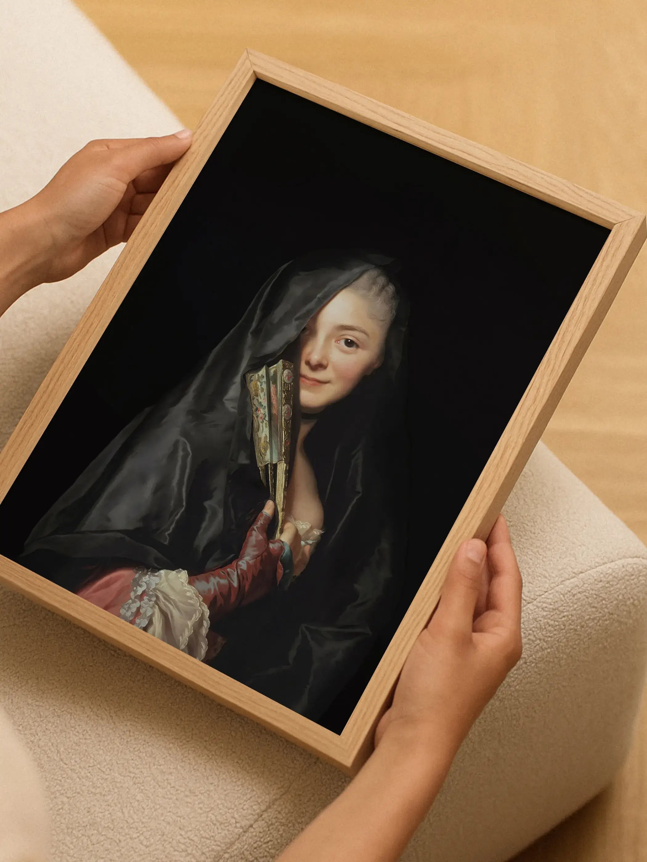 Gerahmtes Dark Academia Porträt mit verschleierter Dame wird von zwei Händen gehalten, im Hintergrund helles Holz und ein beigefarbenes Polstermöbel. Das kontrastreiche Wandbild wirkt edel und moody.