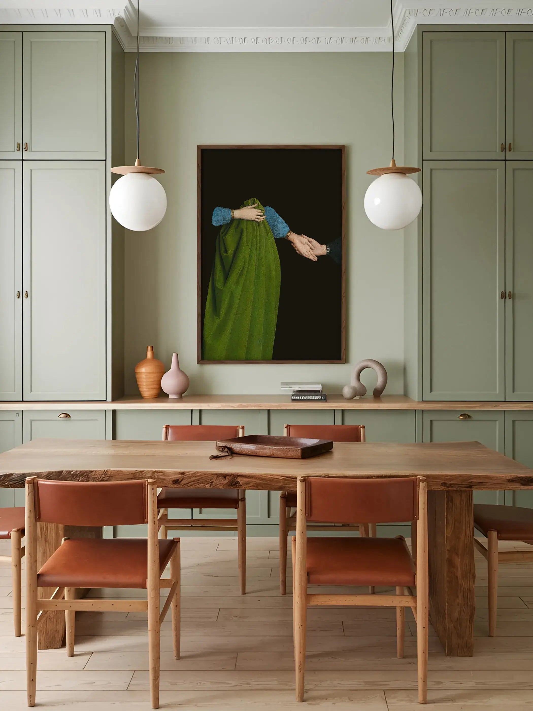 Gerahmter Dark Academia Kunstdruck hängt zwischen zwei Kugelleuchten über einem Holztisch mit Ledersesseln in einer salbeigrünen Küche. Das ruhige Wandbild setzt einen eleganten Akzent im bohemienhaften Esszimmer.