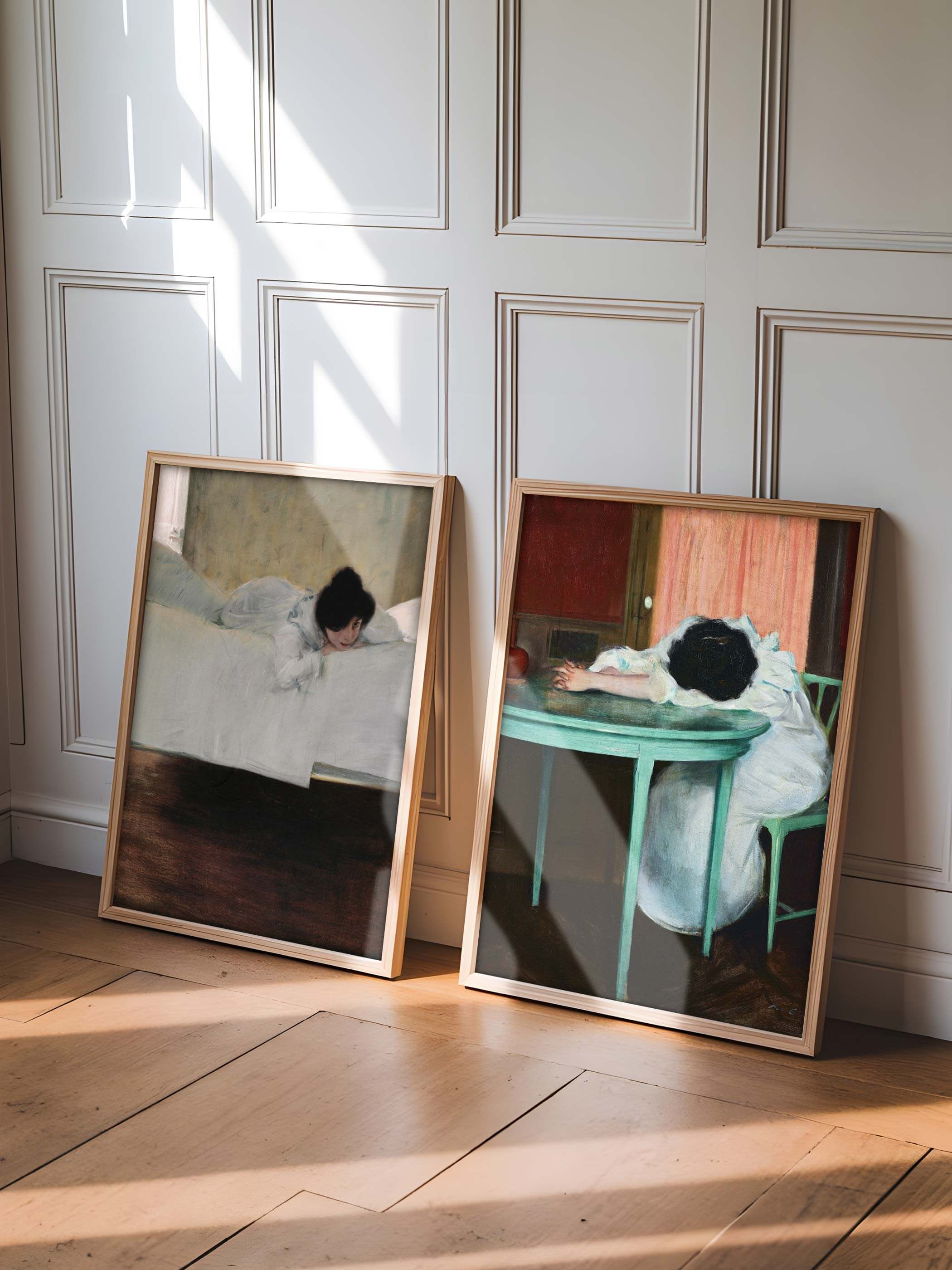 Zwei Vintage-Kunstdrucke mit entspannter Atmosphäre lehnen an einer weißen Wand. Eines zeigt ein Mädchen, das auf einem Bett liegt, während das andere ein Mädchen am Tisch sitzend darstellt. Licht fällt sanft durch das Fenster.
