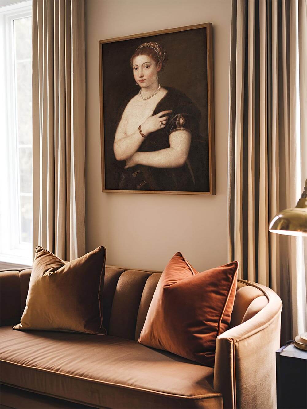Gerahmter Renaissance-Kunstdruck einer Frau mit Perlenkette hängt über samtigem Sofa in warmen Erdtönen. Das Wandbild ergänzt moody und elegante Interieurs mit historischem Charme.