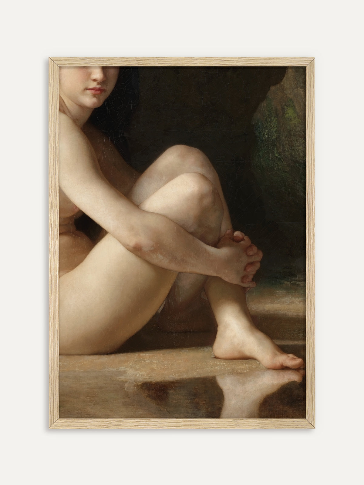 Eine nackte Frau sitzt mit angezogenen Knien am Wasser und umfasst ihr Schienbein, ihr Fuß spiegelt sich in der glatten Wasserfläche, dahinter dunkler Fels. Im Rahmen aus hellem Holz wirkt der klassische Akt ruhig und hell als Wandbild. #Rahmen_Helles Holz