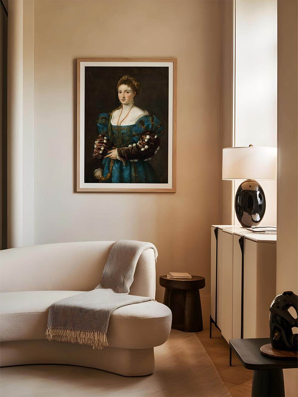 Gerahmter Kunstdruck einer Renaissance-Frau in blauem Kleid hängt über cremefarbenem Sofa. Warmes Licht und moderne Einrichtung schaffen eine harmonische Verbindung von klassischer Kunst und zeitgenössischem Interieur.