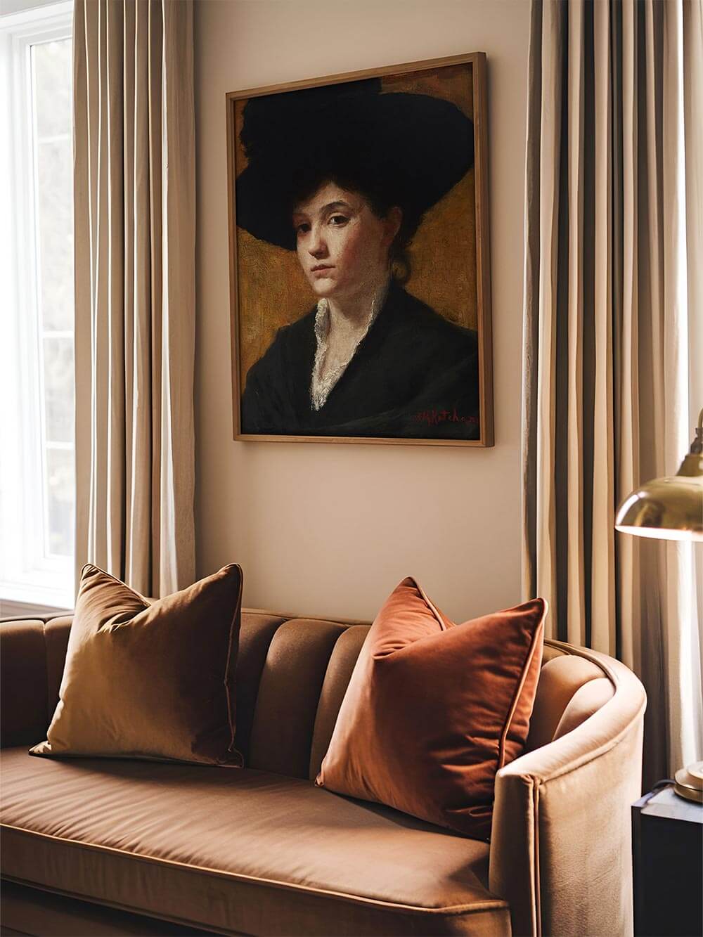 Der gerahmte Kunstdruck mit dem dunklen Damenporträt hängt über einem eleganten Samtsofa im Wohnzimmer. Warme Farben und sanftes Licht schaffen eine nostalgische Atmosphäre.