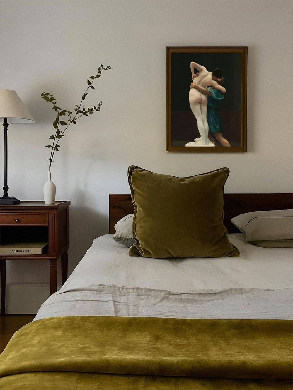 Das gerahmte Dark Academia Wandbild mit klassischem Akt hängt über einem Bett mit olivfarbenem Samt. Es verleiht dem Raum eine sinnlich-elegante Atmosphäre.