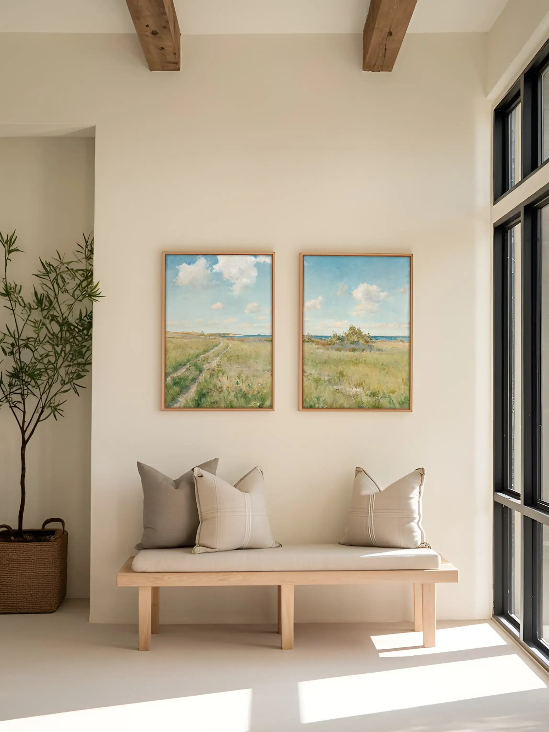 Zwei helle Landschafts-Kunstdrucke mit Wiesenweg, Küste und blauem Himmel hängen über einer Holzbank im minimalistischen Flur. Die sanften Farben und die offene Weite schaffen eine ruhige, natürliche Wandgestaltung im modernen Zuhause.
