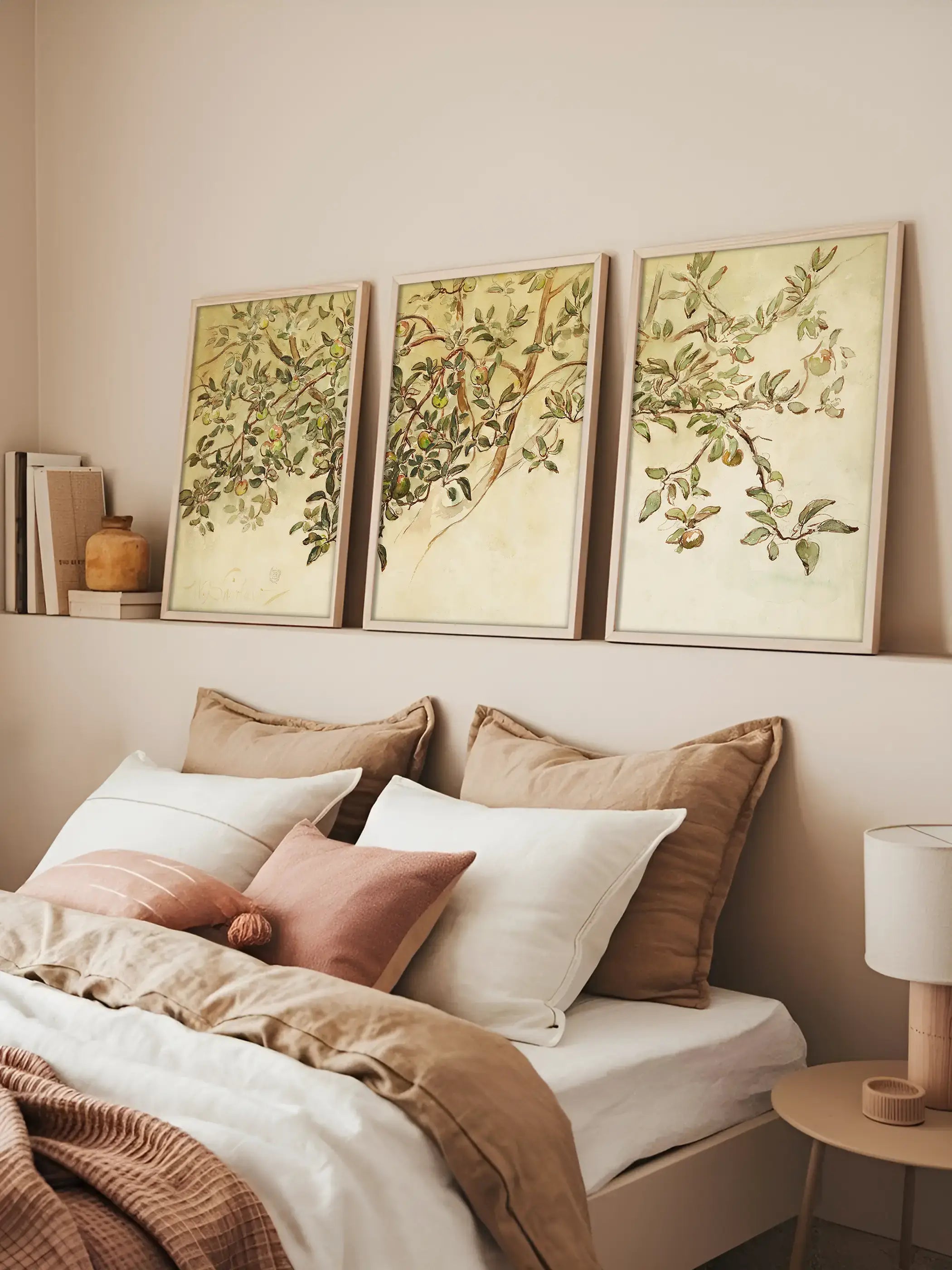 Drei botanische Kunstdrucke mit Apfelzweigen lehnen über dem Bett an einer warmen Wand und schaffen eine entspannte Stimmung. Die Naturmotive passen zu neutralen Schlafzimmern und einer sanften Wandgestaltung.